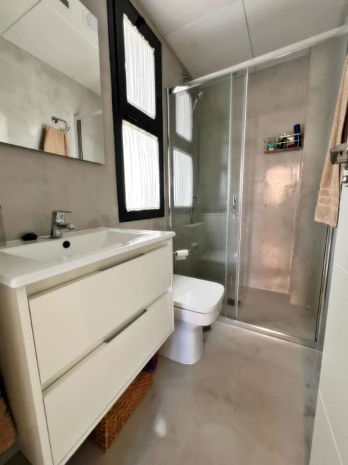 Baño moderno en lujoso apartamento de Fuengirola con tocador blanco, cabina de ducha cristal y luz natural