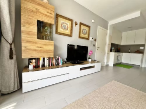 Lujoso salón de apartamento moderno en Fuengirola con panel de pared de madera, consola multimedia blanca y vista a la cocina