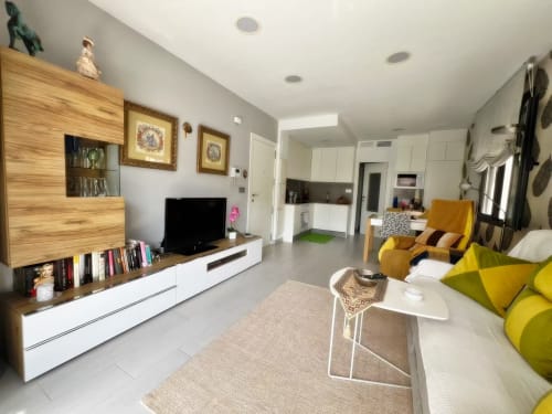 Lujoso apartamento en Fuengirola con salón moderno, mueble TV en madera, asientos amarillos y cocina abierta
