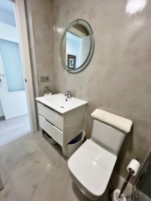 Baño moderno en apartamento de lujo en Fuengirola con tocador blanco, espejo redondo, inodoro y pavimento de baldosa