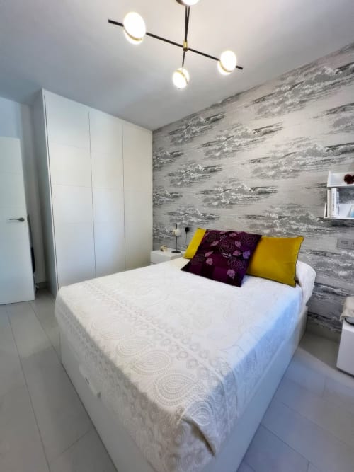 Moderno dormitorio de lujo en Fuengirola con cama blanca, pared de madera gris, almohadas amarillas y techo contemporáneo