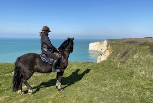 Horseback rider on black horse overlooking turquoise sea and white cliffs near Étretat, Normandy France