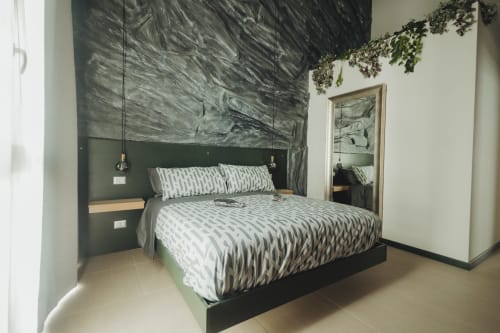 Camera da letto moderna presso Oltre Exclusive a Palermo con testata verde, biancheria a motivi, lampade a sospensione e opere d'arte alle pareti