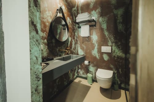 Bagno moderno dell'hotel Oltre Exclusive a Palermo, con pareti dal fascino rustico in tonalità verde, lavabo nero, specchio rotondo e toilette