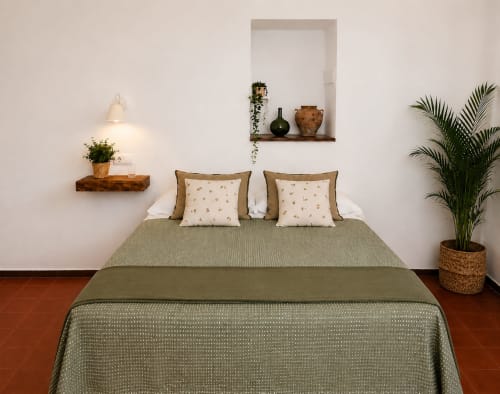 Habitació elegant de l'hotel Mas Ribas a Palamós amb roba de llit verd salvia, plantes en test, prestatges de fusta i sòl de terracota