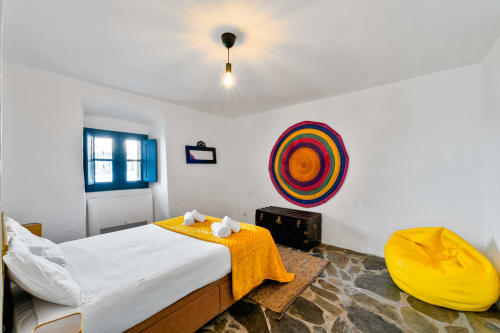 Quarto ensolarado na vila Casa do Loureiro em Alandroal com arte circular colorida na parede, detalhes em amarelo e janela de moldura azul