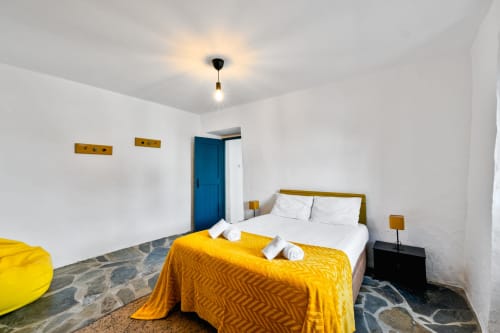 Quarto luminoso na villa Casa do Loureiro em Alandroal com detalhes em amarelo, porta azul e roupa de cama branca