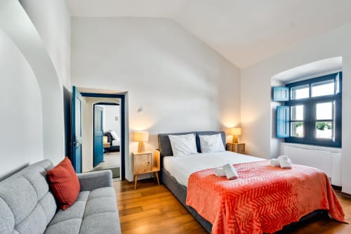 Quarto luminoso na villa Casa do Loureiro em Alandroal com cama, sofá, criados de cabeceira em madeira e janela com moldura azul