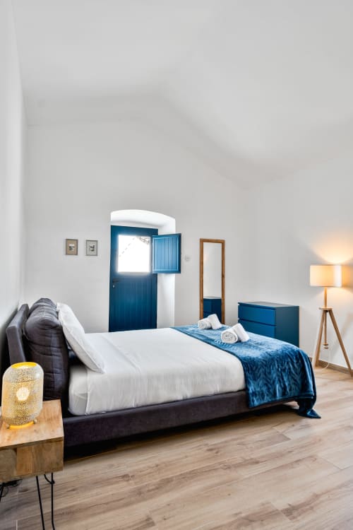 Quarto moderno da villa Casa do Loureiro em Alandroal com paredes brancas, porta azul, piso de madeira e cama escura