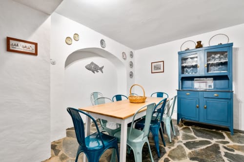 Sala de jantar com vista para o mar na villa Casa do Loureiro, Alandroal, com móveis azuis, mesa de madeira e motivos decorativos de peixe.
