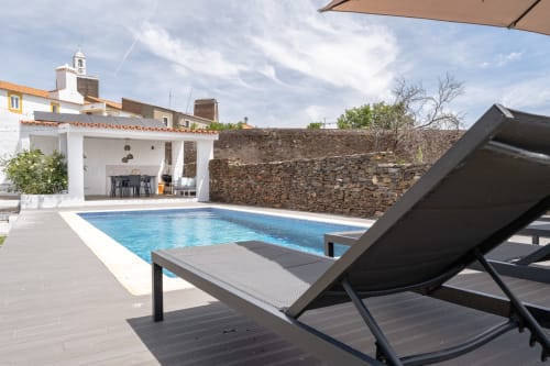 Área de piscina da villa Casa do Loureiro com espreguiçadeiras, pérgola branca e muro de pedra em Alandroal