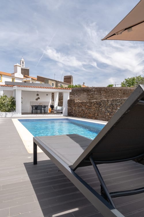 Espreguiçadeira relaxante junto à piscina cintilante na villa Casa do Loureiro em Alandroal, com terraço branco e paredes de pedra