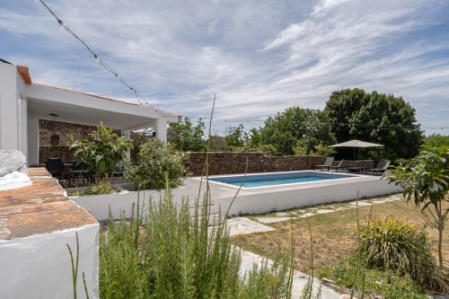Ampla piscina da villa com edifício branco moderno, paredes de pedra, espreguiçadeiras e paisagismo mediterrânico em Casa do Loureiro,