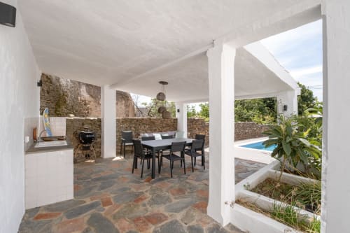 Terraço coberto com mesa de jantar, paredes de pedra, cozinha e vista para a piscina na villa Casa do Loureiro em Alandroal, Portugal