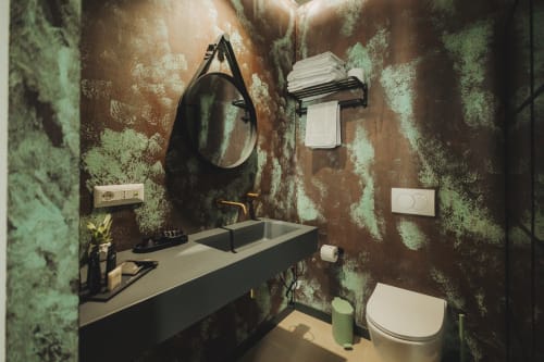 Moderno bagno dell'hotel di Palermo con pareti a motivi teal e bronzo, specchio rotondo nero, doppio lavabo e bidet