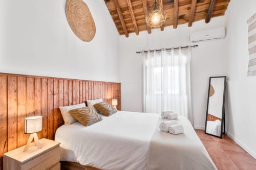Quarto luminoso na Casa do Ti Filipe com cabeceira de madeira, roupa de cama branca, painel de parede tecido e azulejos de terracota rústicos