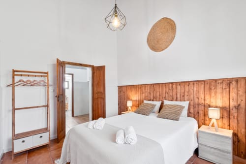 Quarto luminoso da Casa do Ti Filipe com cabeceira de madeira, roupa de cama branca, guarda-roupa de madeira e decoração rústica