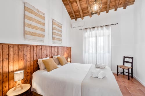 Quarto luminoso na Casa do Ti Filipe com cabeceira em madeira, roupa de cama branca, teto com vigas aparentes e cortinas translúcidas no Airbnb