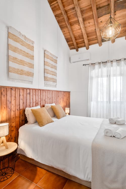 Quarto luminoso na Casa do Ti Filipe com vigas de madeira, paredes brancas, cabeceira de madeira e azulejos em tons de terracota