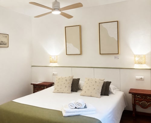 Dormitori modern de l'hotel Mas Ribas a Palamós amb ventilador de sostre, roba de llit blanca, quadres emmarcats i taules de nit de fusta