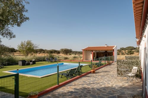 Área de piscina da Casa do Ti Filipe com piscina azul cercada, espreguiçadeiras, pavilhão com telhado vermelho e vistas para a zona rural