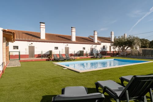 Área de piscina e jardim da Casa do Ti Filipe com espreguiçadeiras, edifício branco com telhado de barro em Montes Juntos, Portugal