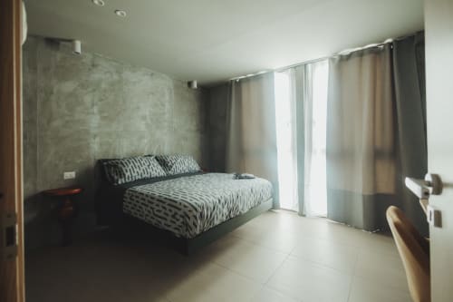 Camera moderna dell'hotel Oltre Exclusive di Palermo con biancheria a motivi, parete in cemento grigio e porte-finestre sul balcone
