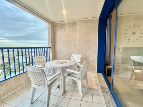 Terraza cubierta con vistas al mar en apartamento de Valencia, muebles de comedor blancos y barandilla azul