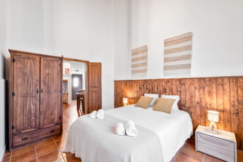 Quarto rústico da Casa da Ti Inácia com cabeceira de madeira, roupa de cama branca e decoração tradicional em Portugal.
