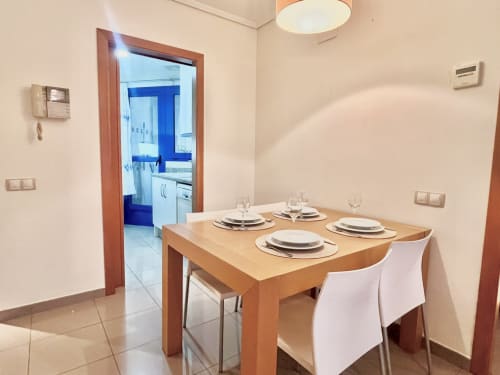 Comedor moderno en apartamento frente al mar en Valencia con mesa de madera, cubiertos y vista abierta a la cocina