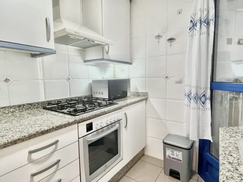 Cocina moderna con vistas al mar en apartamento de Valencia, equipada con estufa de gas, encimeras de granito, gabinetes blancos y acero inoxidable