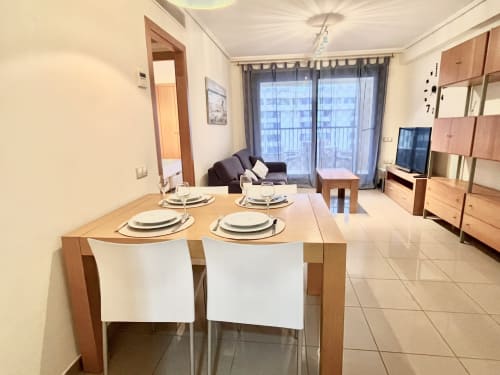 Zona de comedor con mesa de madera y vista al mar en apartamento de Valencia con sala de estar y acceso a balcón