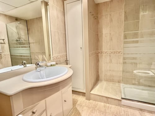 Baño moderno con azulejos beige, lavabo redondo, espejo y ducha con mampara de cristal en el apartamento Pataconablue con vista al mar