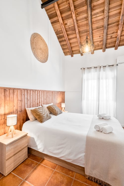 Quarto rústico da Casa da Ti Inácia com teto de vigas de madeira, tapeçaria tecida na parede, roupa de cama branca e piso de ladrilhos de terracota