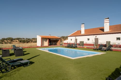 Piscina da Casa da Ti Inácia com espreguiçadeiras, jardim bem cuidado e villa branca com telhado de barro na zona rural portuguesa
