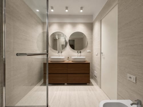 Bagno moderno della Suite Ingrid alle SEVEN SUITES SANREMO con doppi lavabi a bacinella, specchi circolari, vanity in legno e rivestimento in piastrelle
