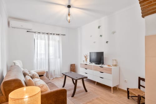 Moderno estúdio na Casa da Ritinha com confortável assento, TV, móveis de madeira e muita luz natural
