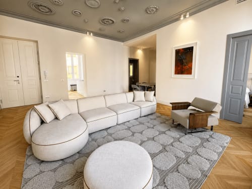 Soggiorno moderno alle SEVEN SUITES SANREMO con divano curvo color crema, poggiapiedi rotondo e pavimenti in legno nella Suite Ingrid