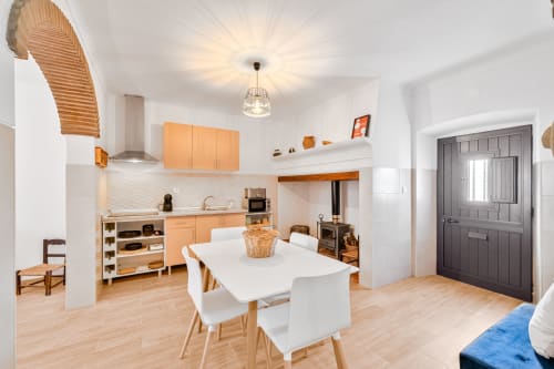 Moderna cozinha integrada e sala de jantar em Casa da Ritinha com armários de madeira, mesa branca e lareira em Montes