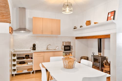 Cozinha e área de refeições modernas no apartamento Casa da Ritinha com armários de madeira, bancadas brancas e mesa de jantar