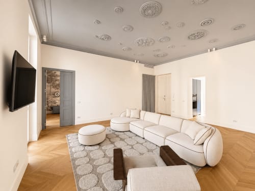Soggiorno moderno nella Suite Ingrid dei Seven Suites Sanremo con divano bianco curvo, dettagli decorativi al soffitto e pavimento in legno