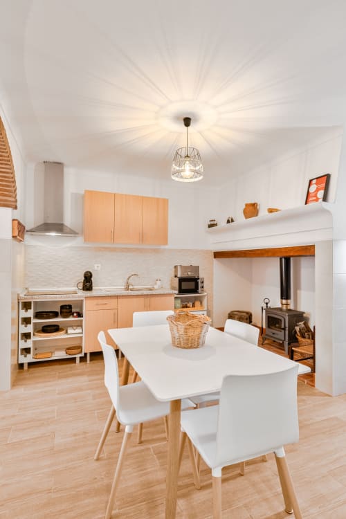 Cozinha e sala de refeições modernas da Casa da Ritinha com mesa branca, cadeiras de madeira, armários em madeira clara e fogão em ambiente luminoso