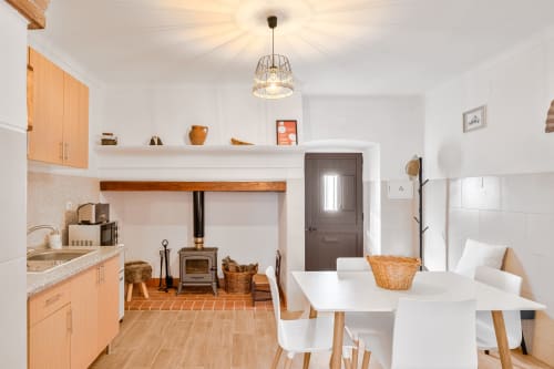 Aconchegante cozinha integrada e sala de refeições na Casa da Ritinha com fogão a lenha, mesa de jantar branca e mobiliário em madeira natural.