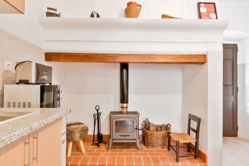 Cozinha e sala aconchegantes na Casa da Ritinha com fogão a lenha, vigas rústicas, azulejos de terracota e móveis de vime.