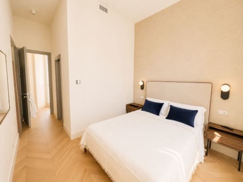 Camera moderna della Suite Ingrid presso Seven Suites Sanremo con letto bianco, cuscini blu navy, pavimenti in legno e vista sulla città
