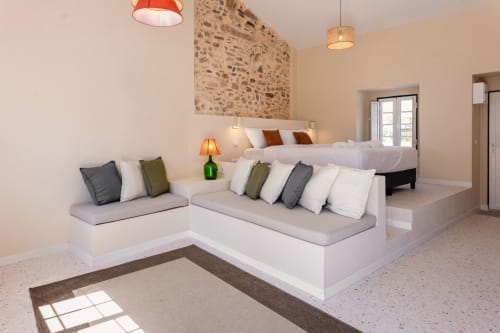Modern bedroom with seating area at FC Housing Company in Abrantes, featuring white built-in seating, stone accent wall, and