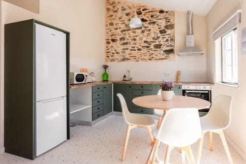 Modern kitchen and dining area in Abrantes apartment with green cabinetry, stone accent wall, wooden table, and white chairs