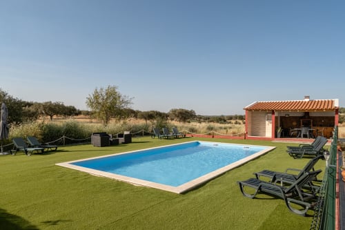 Piscina da Casa da Ritinha com água azul, gramado verde, espreguiçadeiras e casa com telhado vermelho em Montes Juntos, Portugal