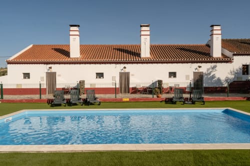Piscina da Casa da Ritinha com espreguiçadeiras, edifício branco com detalhes vermelhos, telhado de barro, Montes Juntos, Alentejo Portugal