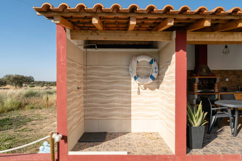 Chuveiro exterior da Casa da Ritinha com boia de salvação, telhado de barro e zona de refeições no pátio da propriedade rural no Alentejo